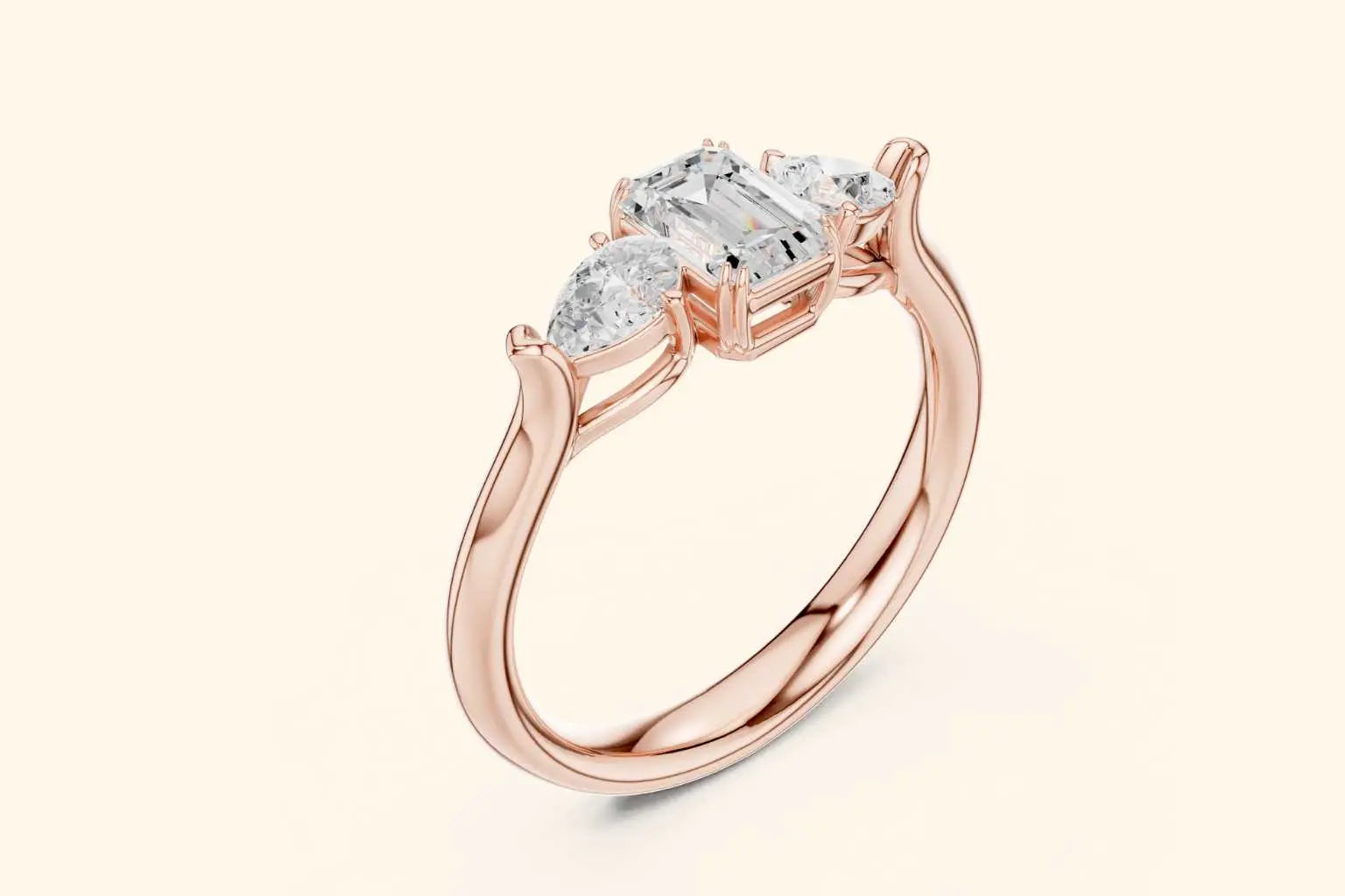 An angled view of a three-stone ring in high-polished rose gold. The central emerald-cut diamond and two side pear-shaped diamonds are held by elegant, flowing prongs that merge into the slender band.