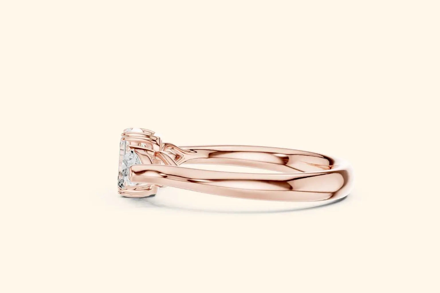 A close-up horizontal side view of a wide-band three-stone ring in polished rose gold. The view emphasizes the low-profile setting where the emerald and pear-cut diamonds sit close to the finger.