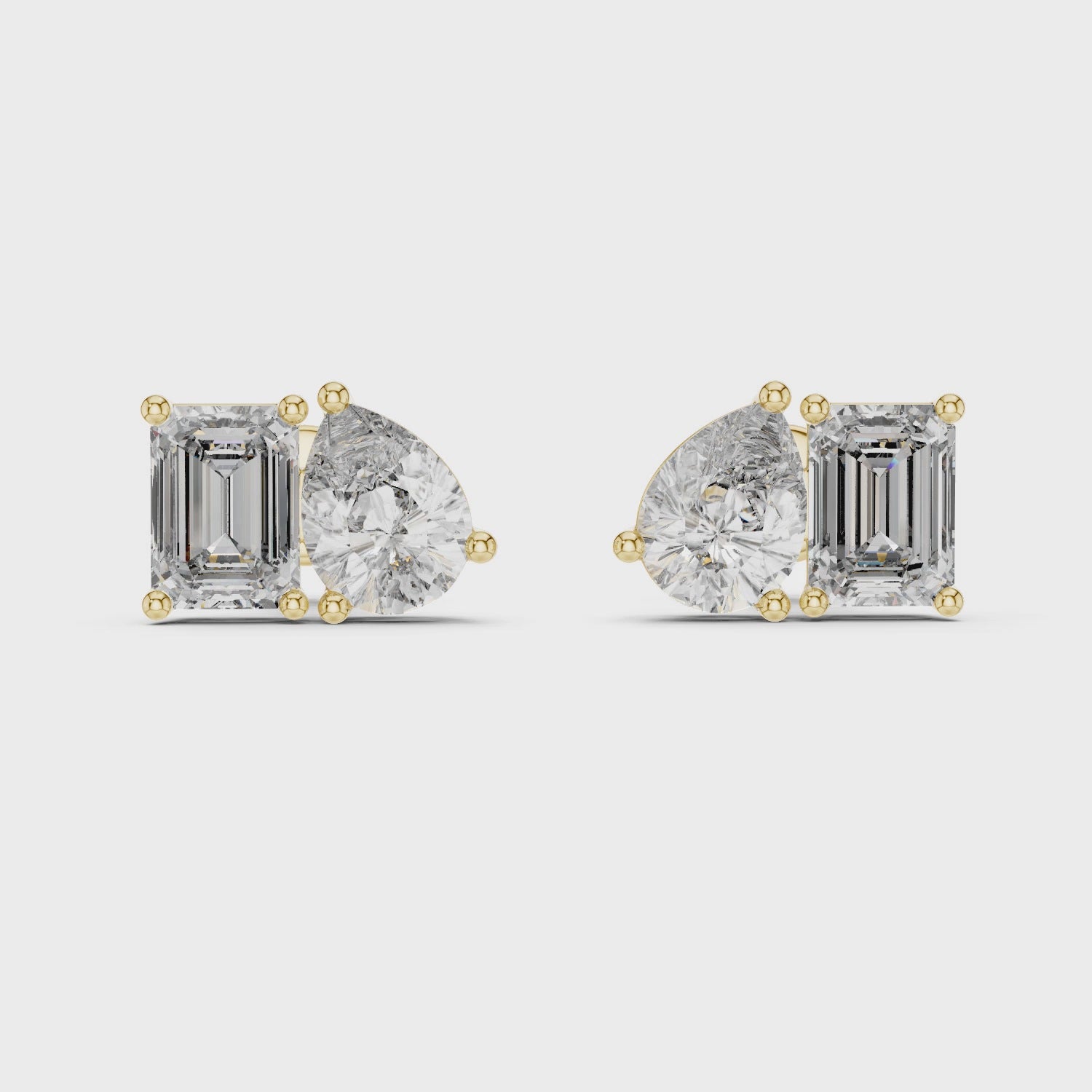 Pair of yellow gold stud earrings featuring a cluster of one pear-cut and one emerald-cut diamond