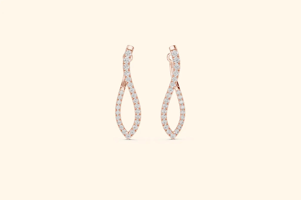 Pair of rose gold twisted infinity drop earrings with pave diamonds on a pale background