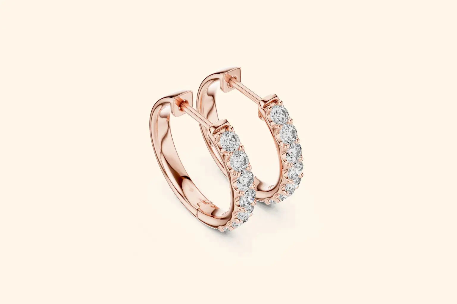 Pair of rose gold diamond huggie hoop earrings with prong setting viewed at a slight angle on a pale background