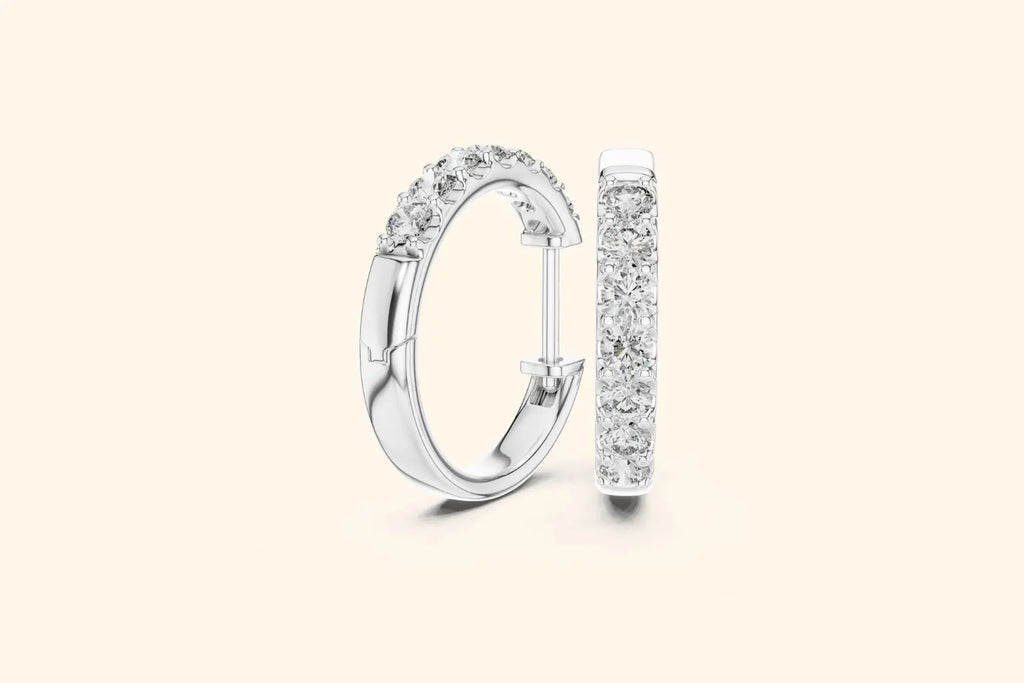 Pair of silver diamond huggie hoop earrings with prong setting on a pale background