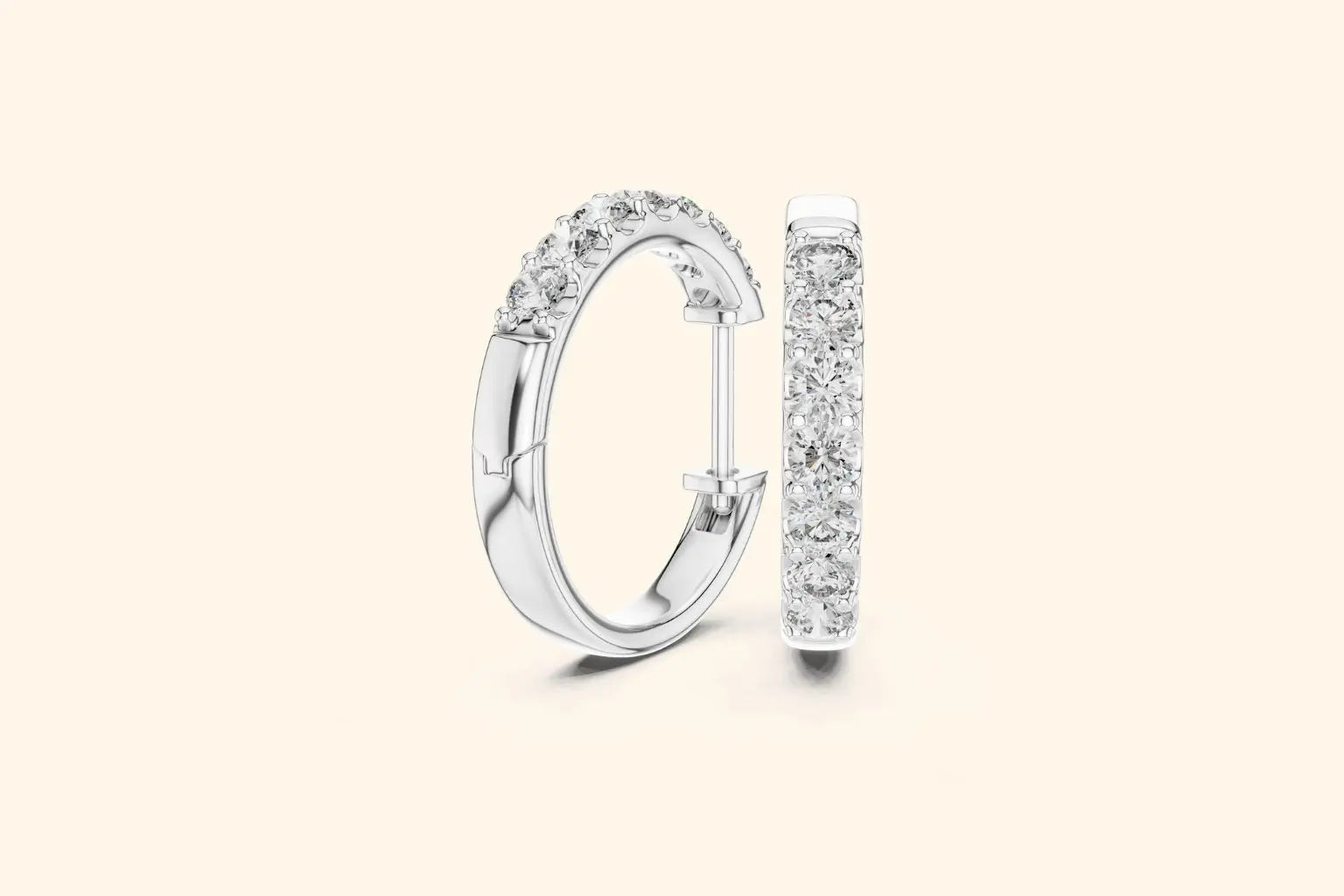 Pair of silver diamond huggie hoop earrings with prong setting on a pale background