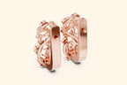 Rose gold hoop earrings with intricate designs on a light beige background