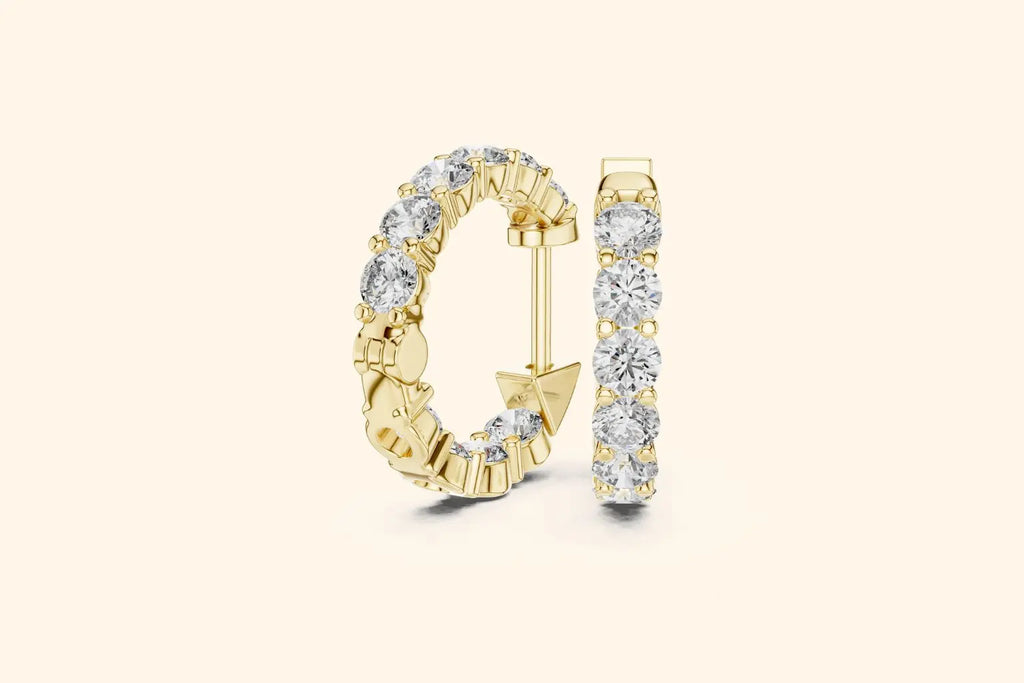 Pair of yellow gold large round diamond eternity hoop earrings with gallery setting on a pale background
