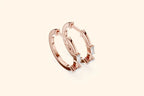Rose gold hoop earrings with small diamonds on a light beige background