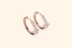 Rose gold hoop earrings with clear gemstones on a light beige background