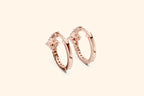 Pair of rose gold hoop earrings on a light pink background