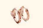 Rose gold hoop earrings with floral designs on a light beige background