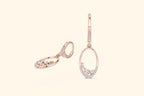 Rose gold earrings with diamond accents on a light pink background