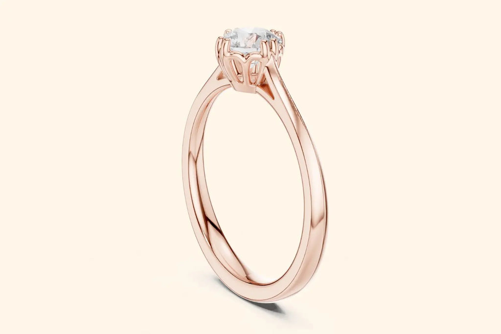 Close-up side view of a rose gold solitaire ring showing a four-prong setting with filigree accents and a thin, tapered band. The round diamond is slightly visible.