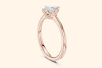 A side view of a simple, thin, polished rose gold ring band flowing up to a high-set, square diamond setting.