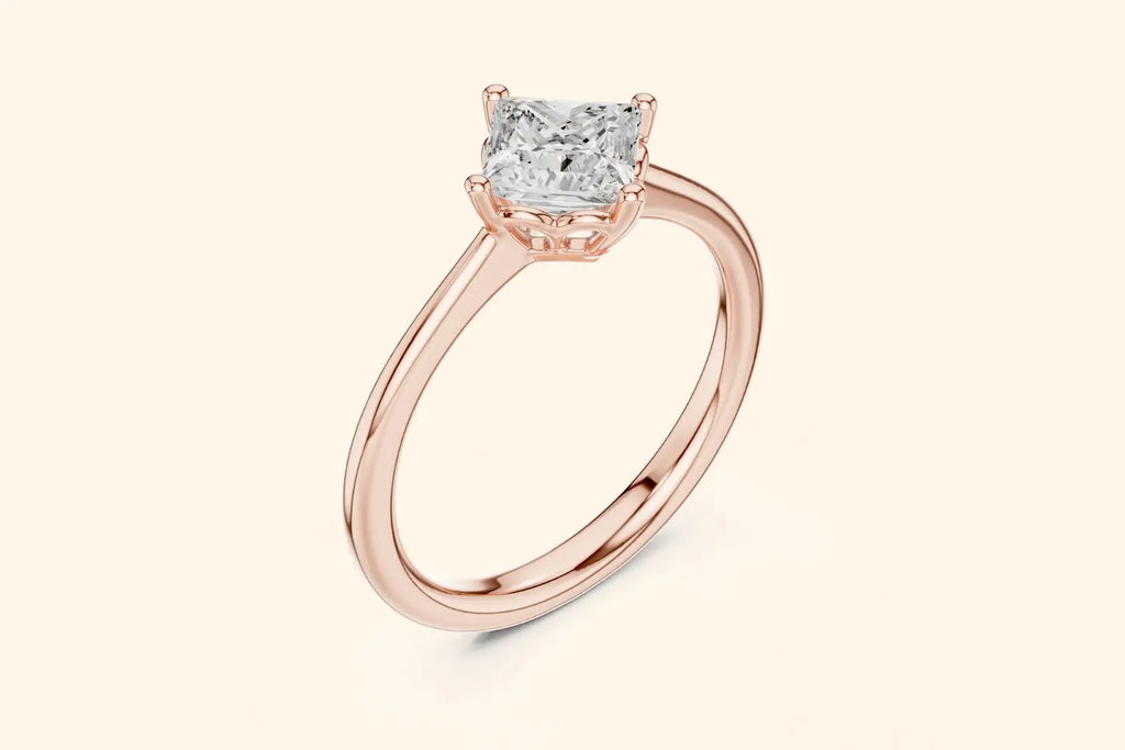 A three-quarter view of a delicate rose gold solitaire ring with a high-set, square-cut diamond, showing a low-profile basket setting.