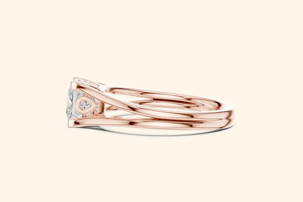 A side profile of a rose gold engagement ring, showing the low-profile setting, the ornate gallery design, and the smooth, split-shank band.