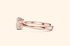 Side profile view of a polished rose gold engagement ring, showcasing the smooth band and the ornate, six-prong basket setting holding the oval diamond.