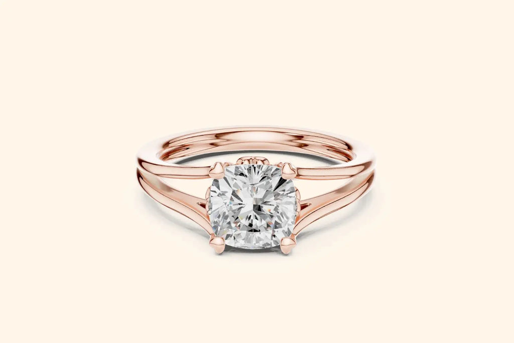 A modern solitaire ring featuring a cushion-cut diamond set on a wide, elegant split-shank band in polished rose gold.