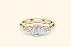A head-on view of a stunning three-stone ring in rich pure gold or yellow gold. The centerpiece is a large emerald-cut diamond, accented by a pear-shaped diamond on either side, set on a polished, substantial band.