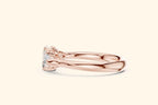 A close-up horizontal side view of a wide-band three-stone ring in polished rose gold. The view emphasizes the low-profile setting where the emerald and pear-cut diamonds sit close to the finger.
