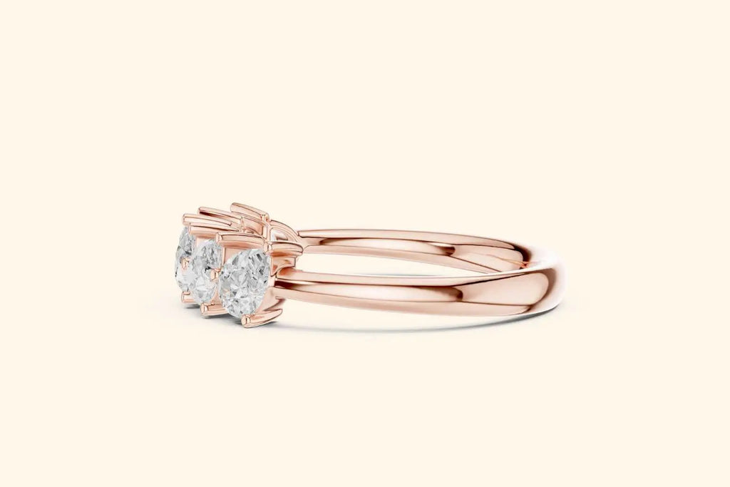 A horizontal side view of a half-band ring in polished rose gold. The shot emphasizes the setting, showing the cluster of pear-shaped diamonds and the sleek, smooth curve of the ring's band.