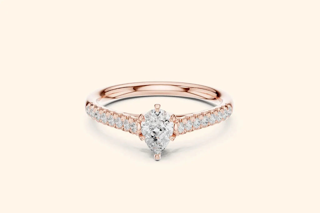 A delicate rose gold engagement ring with a brilliant pear-cut diamond in the center and pave diamonds running down the shank.