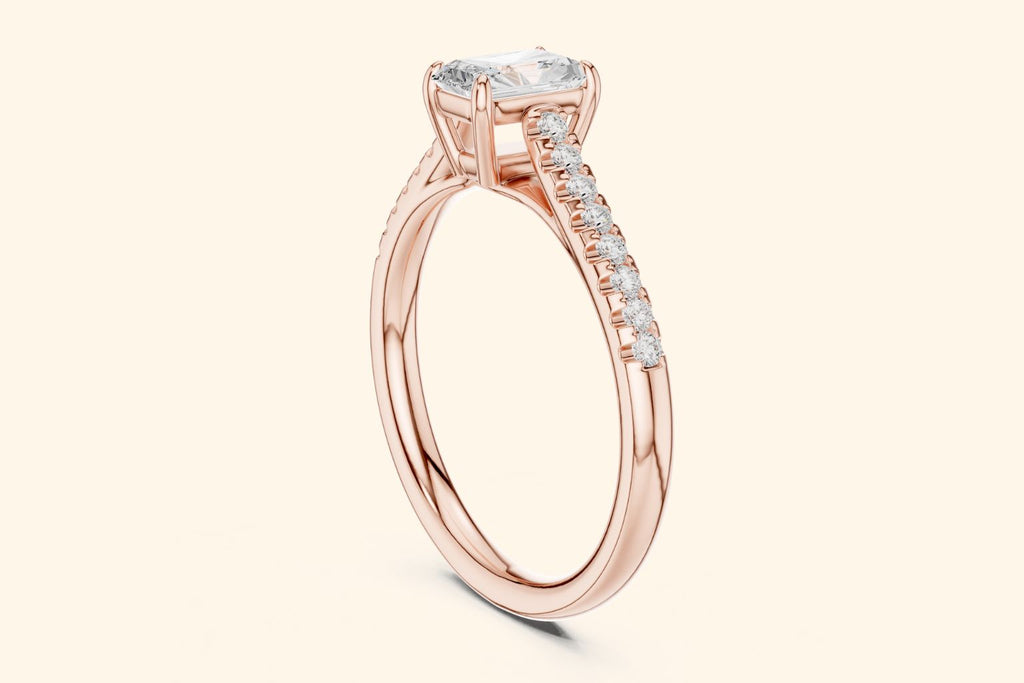 Rose gold engagement ring with a radiant-cut center diamond and a pavé band of small diamonds on each side.