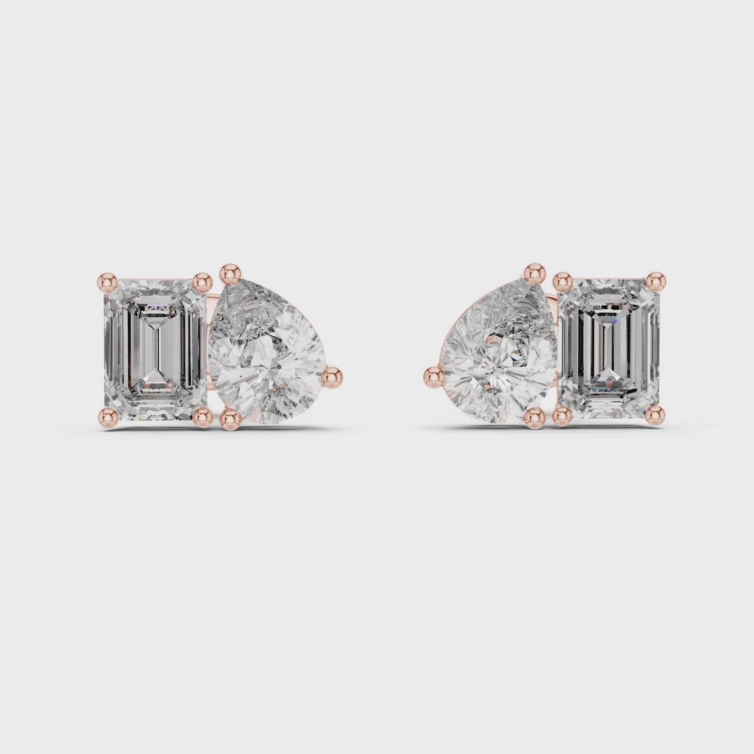 Pair of rose gold mismatched diamond stud earrings featuring one emerald cut and one pear cut diamond on a white background